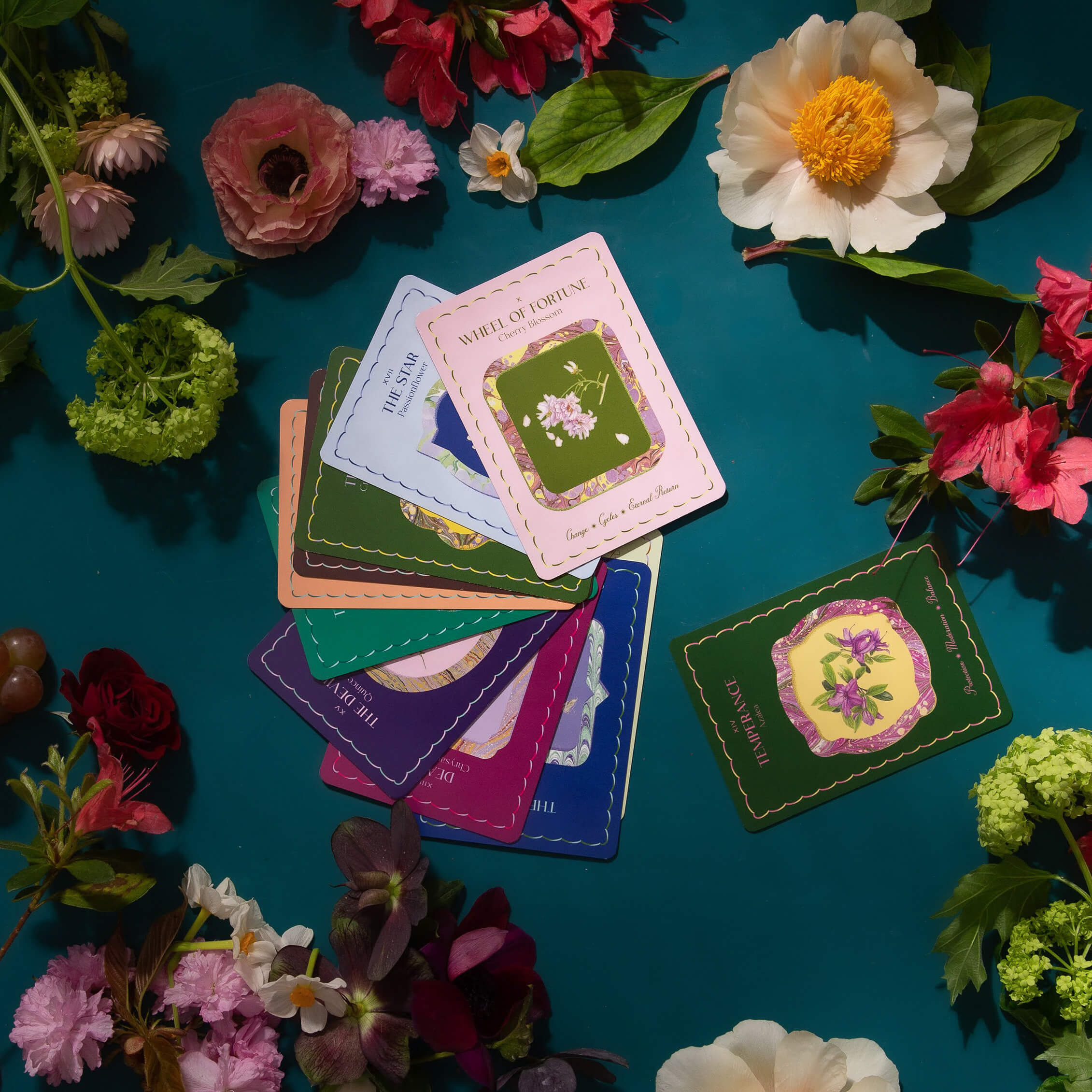 A hand of The Garden Journey cards lies fanned out on a beautiful flower-strewn table.